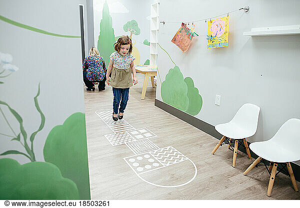 Little girl jumps on a hopscotch inside an educational facility