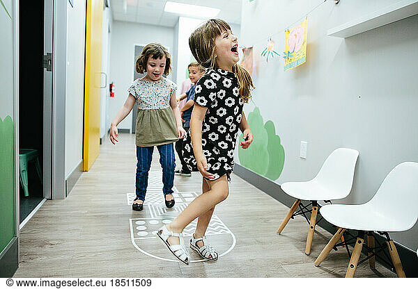 Little girl laughs as she plays hopscotch in a hallway