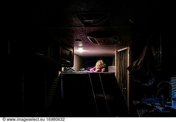 little girl laying on top bunk reading during a camping trip