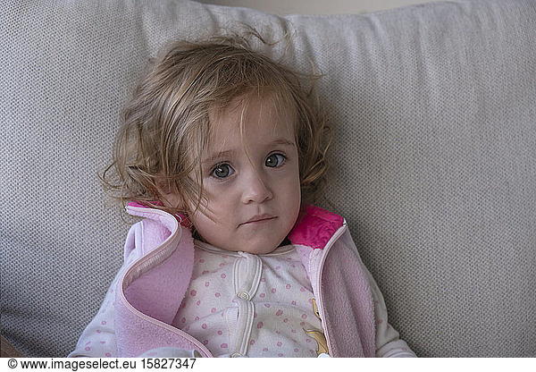 Little girl looking at the camera  on the couch in her living room.