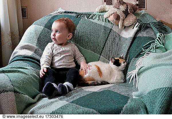little girl looking at window while siiting in armchair with cat