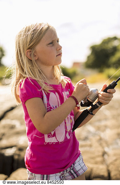 Little girl looking away while holding fishing rod outdoors