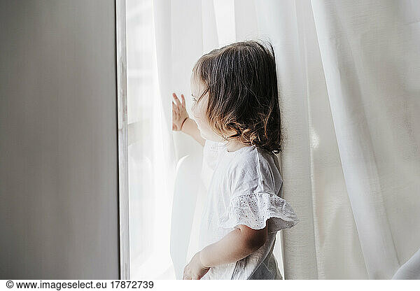 Little girl looking out of window at home
