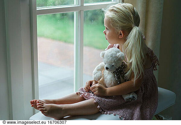 Little girl looking sadly out the window watching rain.