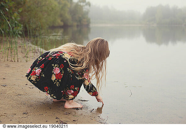Little girl on a lonesome and foggy adventure dips finger in pond