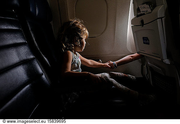 little girl on airplane holding hands with sister in other aisle