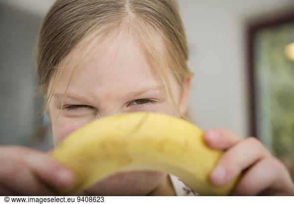 Little girl peeking behind banana