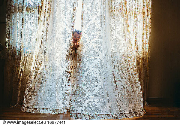 Little girl playing hide and seek with big vintage curtains at home