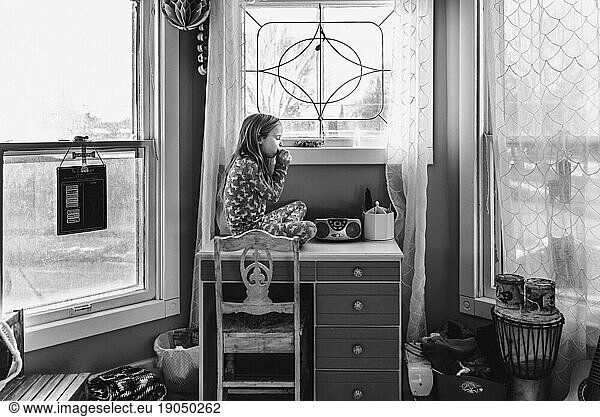 Little girl plays harmonica in bedroom while sitting on top of desk