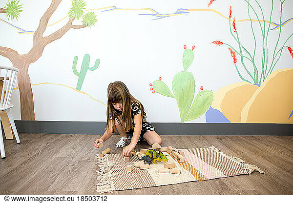 Little girl plays on the ground with blocks and dinosaurs