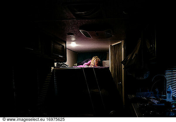 little girl reading at night on top bunk in travel trailer camping