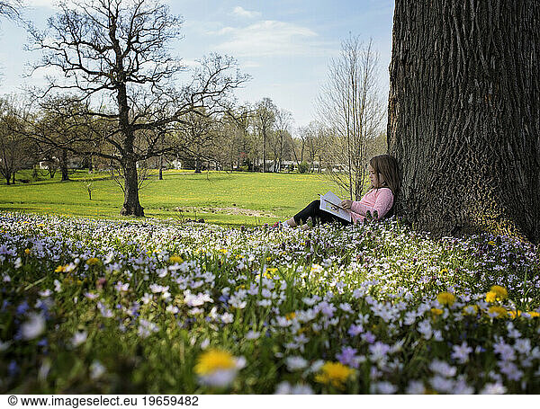 Little girl reading in field of flowers