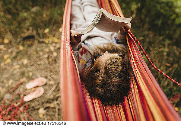 Little girl reads a book in hammock on a warm fall day while camping