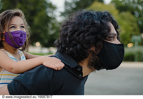 little girl riding piggyback on with her dad wearing face masks