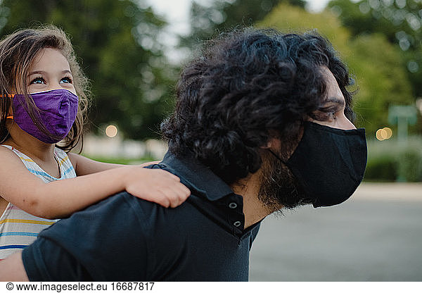 little girl riding piggyback on with her dad wearing face masks little ...