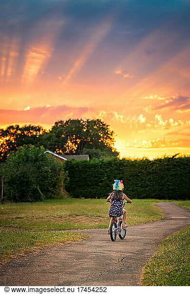Little girl riding with a unicorn helmet riding bicycle at sunset