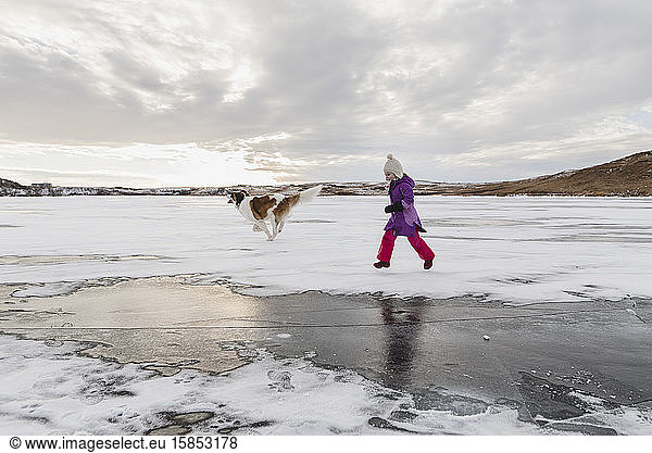 Little Girl Runs on Frozen Lake with Dog