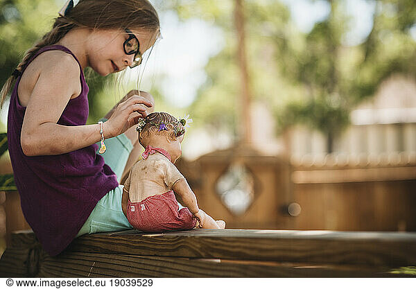 Little girl sits in backyard with vintage doll on a warm day