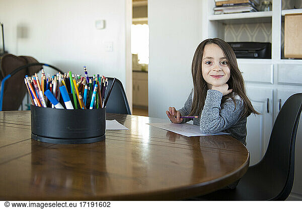 Little Girl Sitting at a table with paper and pencil.