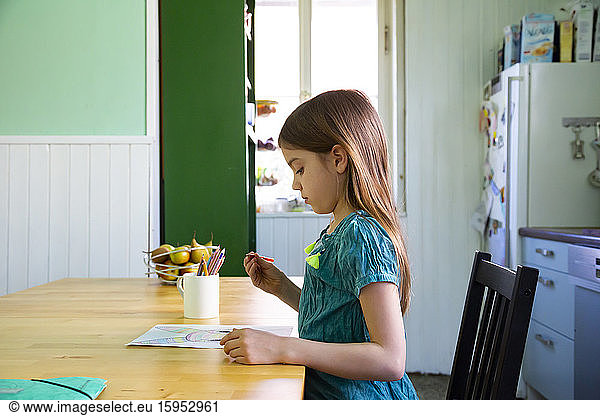 Little girl sitting at kitchen table  drawing an Easter bunny