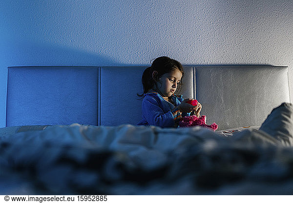 Little girl sitting on bed playing with her toy