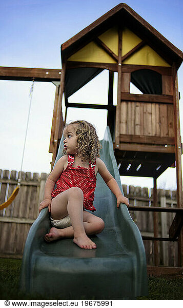 Little girl sliding on playground in red swim suit