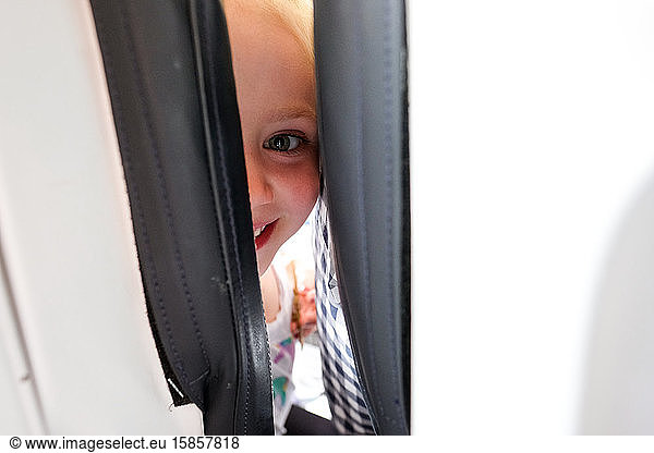 little girl smiling and looking at camera between seats on airplane