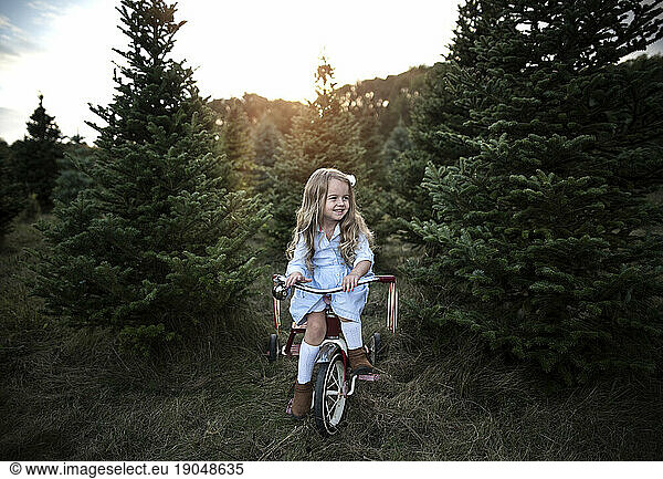 Little girl smiling on bike with Christmas trees