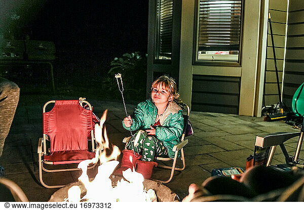 little girl smiling while sitting in front of fire pit eating