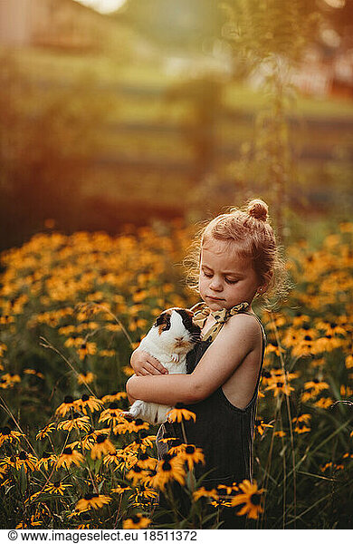 little girl snuggling her pet guinea pig in a field of flowers