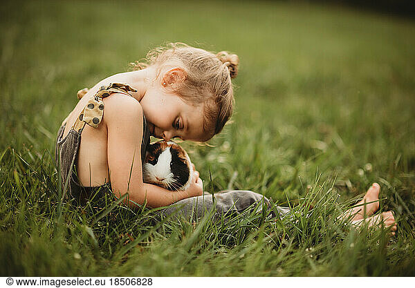 little girl snuggling her pet guinea pig in the grass