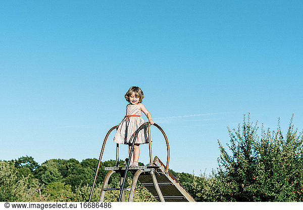 Little girl standing on top of a slide and feeling tall and brave