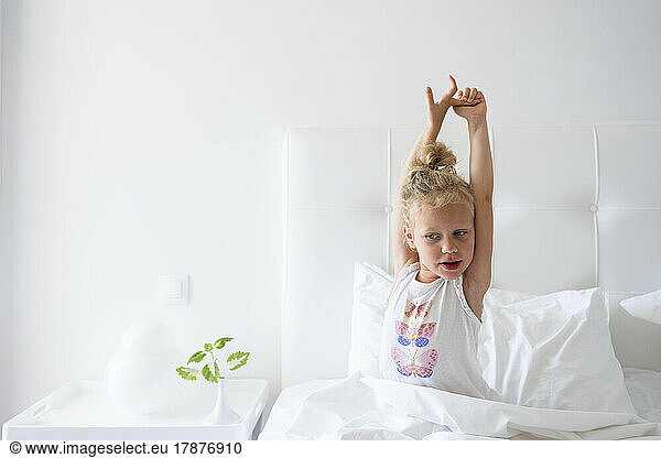 Little girl stretching arms sitting in bed