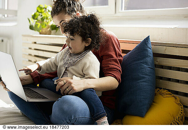 Little girl using laptop sitting on lap of mother on couch at home