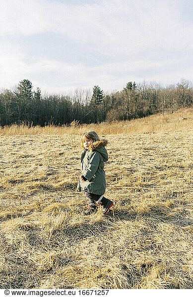 Little girl walking through a field in the wintery evening sun.