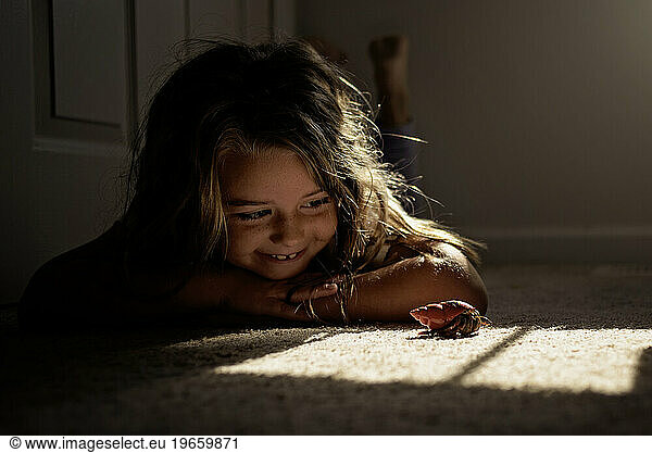 Little girl watching hermit crab crawl on carpet