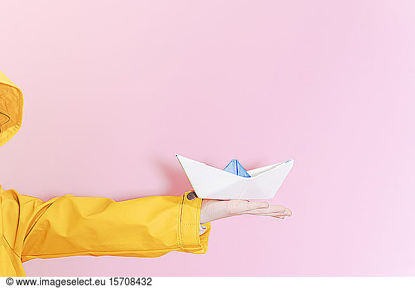 Little girl wearing an oilskin and holding a paper boat on her outstretched arm