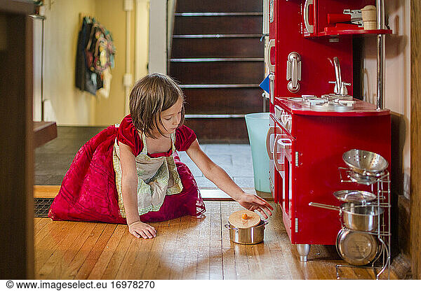 little girl wearing apron and party dress plays with toy kitchen
