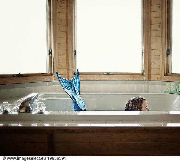 Little girl wearing blue mermaid tail in spa tub