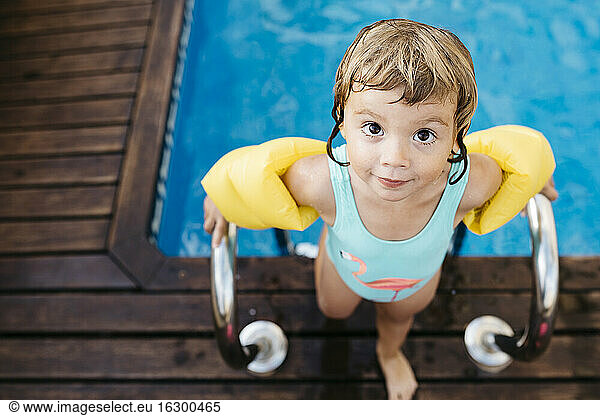 Little girl with armbands at ladder of swimming pool