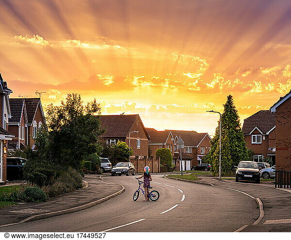 Little girl with bicycle and unicorn helmet looking at stunning sunset