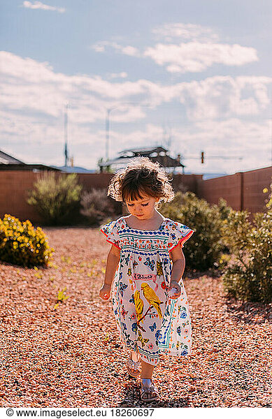 Little girl with curly hair walking outside in a colorful dress