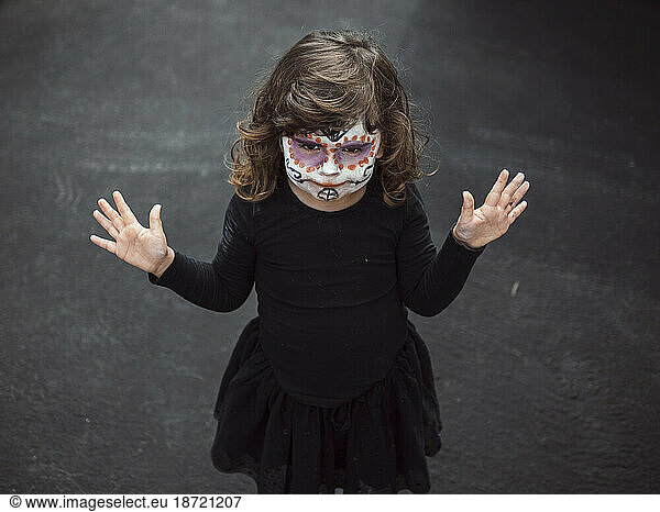 Little girl with face painted and disguised for halloween with hands u