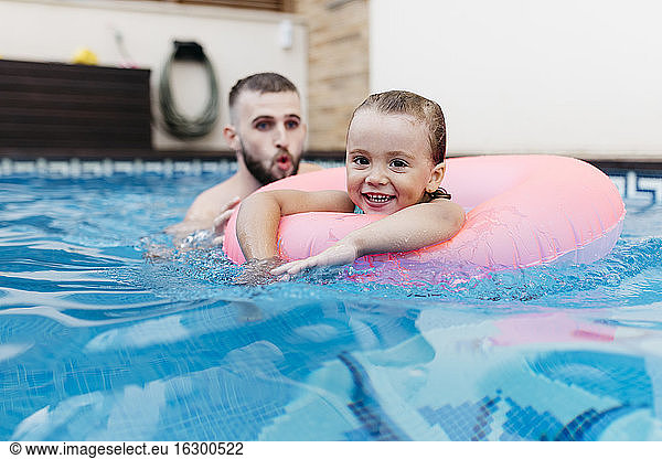 Little girl with floating tire and her uncle in swimming pool