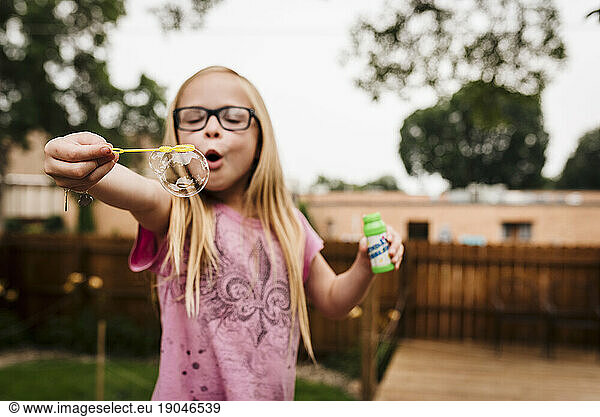 Little girl with glasses blows bubbles in North Dakota backyard summer