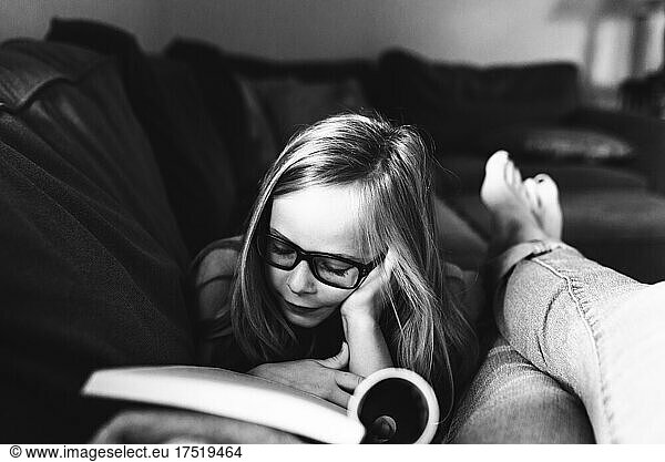 Little girl with glasses reads on sofa with mom