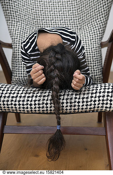 Little girl with long braid crouching on an armchair