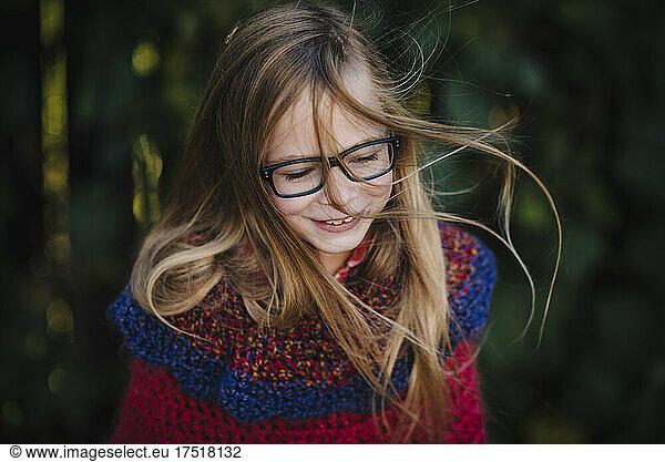 Little girl with long hair and glasses swings hair joyfully outdoors
