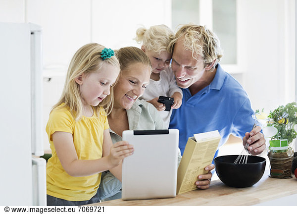Little girl with parents using digital tablet for recipe in kitchen