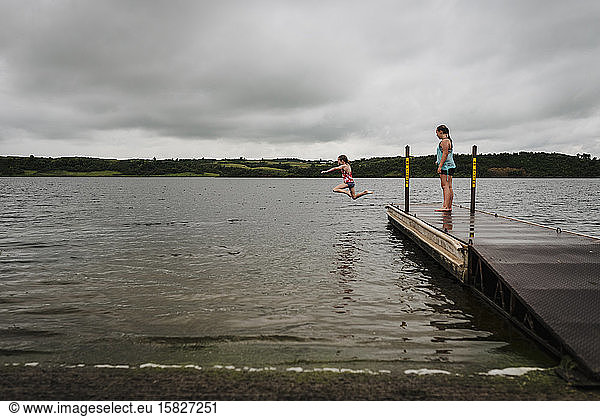 Little Girls Jump off Dock into Lake on a Cloudy Summer Day